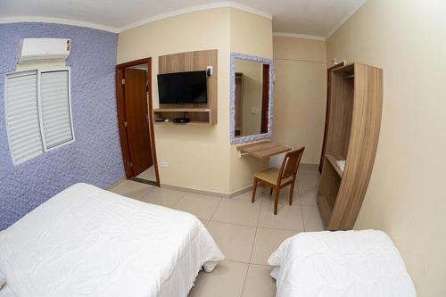 a bedroom with two beds and a desk and a television at Aeroporto Plaza Hotel in Campo Grande