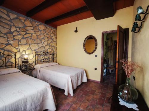 1 dormitorio con 2 camas y pared de piedra en Casa Rural El Tejar Viejo, en Carcabuey