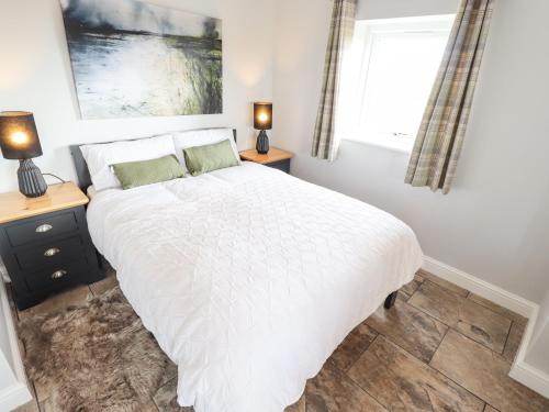 a bedroom with a white bed and two night stands at Sanderlings Cottage in Mablethorpe