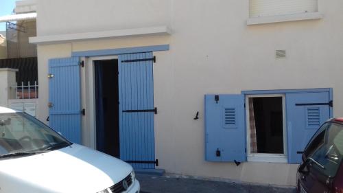 une voiture blanche garée devant un bâtiment avec portes bleues dans l'établissement Hippocampe - Jolie petite Maison de vacances à la Corniche, à Sète