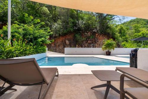 a swimming pool with two chairs and a table at Bello Departamento Veleros frente al mar in Acapulco