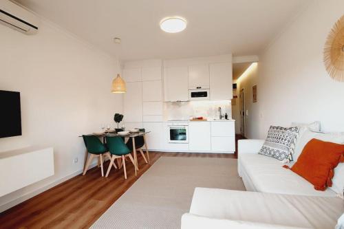 a living room with a white couch and a kitchen at Lindo apartamento junto à praia e à Marina de Vilamoura com Piscina e Wi-Fi in Quarteira