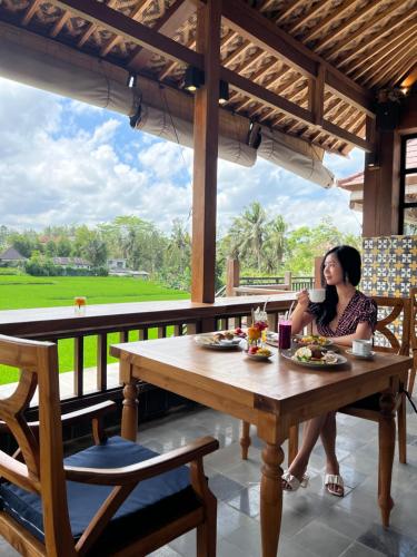 a woman sitting at a wooden table on a porch at Danakha Villa Ubud in Tegalalang