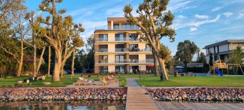 a building with people sitting on benches in front of a body of water at Platán Beach Apartman in Balatonboglár