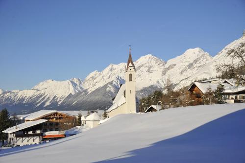 a white church with snow covered mountains in the background at Hotel Lärchenhof Natur in Seefeld in Tirol