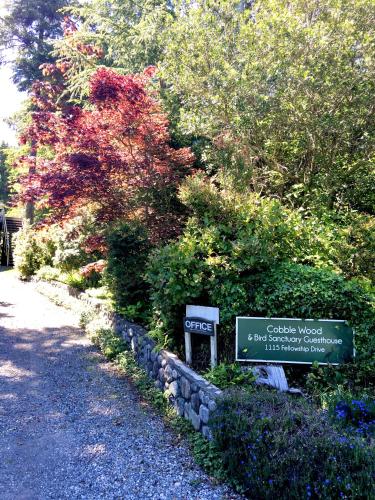 a sign for a garden in front of some bushes at Cobble Wood and Bird Sanctuary Guest Houses in Tofino