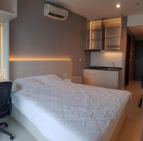 a bedroom with a large white bed and a kitchen at Apartemen Borneo Bay City (1 Bedroom Studio) in Klandasan Kecil