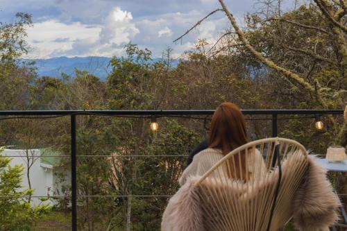 una donna in piedi su un balcone che guarda le montagne di AKOA GLAMPING Eco-Luxury Hotel a Guarne