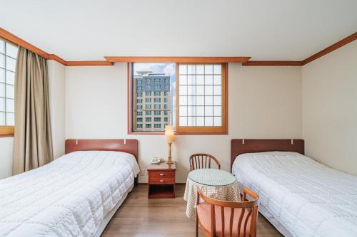 two beds in a room with a table and two windows at Samhaein Tourist Hotel in Jeju