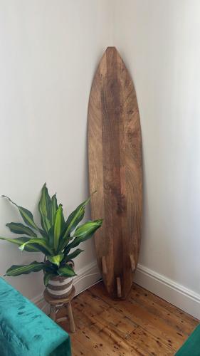 a wooden surfboard leaning against a wall with a potted plant at Casa Cozy in Torquay