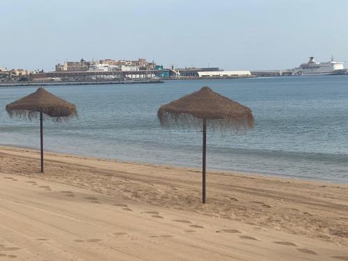 two straw umbrellas on a beach with the water at Precioso apartamento a 50 metros de la playa in Melilla