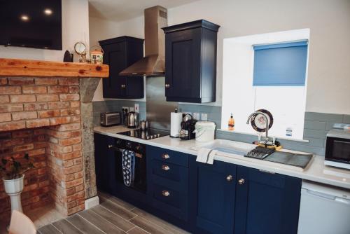 cocina con armarios azules y chimenea de ladrillo en Lizzie's Cottage, en Drumaroad