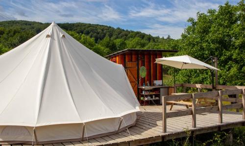 a white teepee on a wooden deck with a bench and an umbrella at Dolina Village Glamping in Zece Hotare