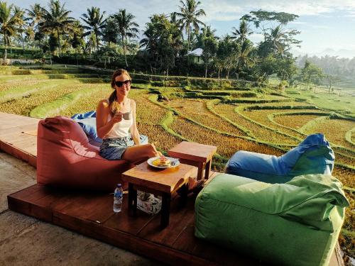 a woman sitting on a couch in front of a field at Peraja Bungalows Loyok in Sangyang
