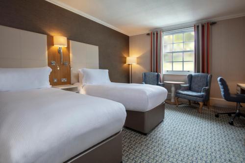 a hotel room with two beds and a desk at Oulton Hall Hotel, Spa & Golf Resort in Leeds