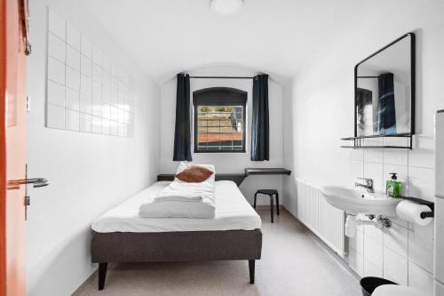 een kleine witte kamer met een bed en een wastafel bij Fengselshotellet in Arendal