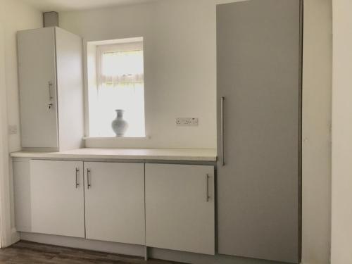a white kitchen with white cabinets and a window at Cree River Cottage in Creegh