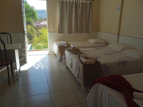 a room with three beds and a table and a window at Pousada Delícias do Mar in Pirenópolis