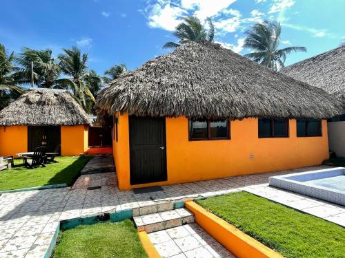 an orange house with a thatched roof and a pool at Johnnys Place Hotel in Monterrico