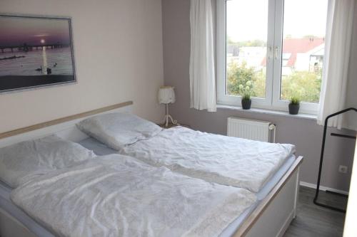 1 cama blanca en un dormitorio con 2 ventanas en Grüntal Residenz I Whg 6, en Grömitz