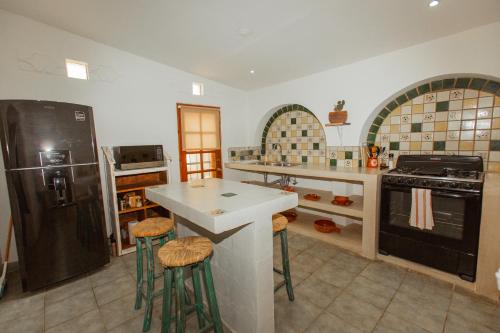 a large kitchen with a black refrigerator and stools at Cien Palmas- Authentic Mexican Casita 1 -Downtown in Todos Santos