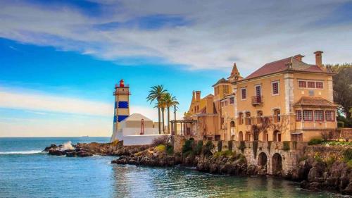 a building and a lighthouse next to the ocean at Happy Holiday Cascais - Garden in Cascais