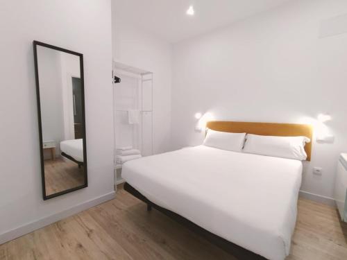 1 dormitorio con 1 cama blanca grande y espejo en Apartamentos La Brava by gaiarooms, en Salamanca