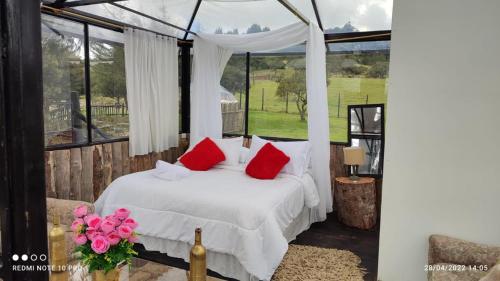 1 dormitorio con cama blanca y almohadas rojas en Tu Glamping en Chocontá