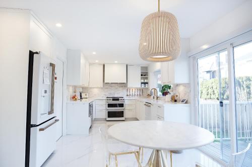 a white kitchen with a table and a pendant light at Steveston Village Bed and Breakfast in Richmond