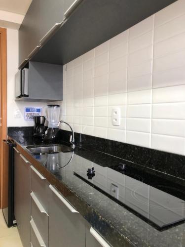 a kitchen with a black counter top and white tiles at » MODERNO E ACONCHEGANTE FLAT COM VARANDA « in João Pessoa