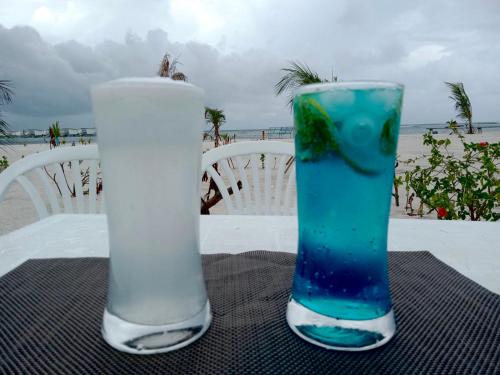 dos vasos de beber sentados en una mesa con la playa en La Isla Tropica en Guraidhoo