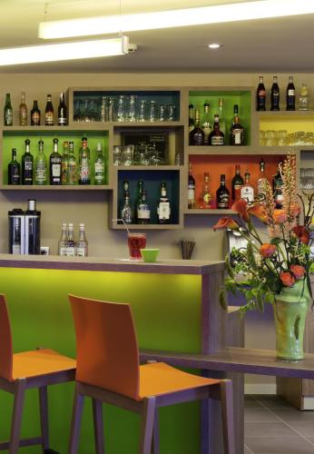 a bar with green and orange chairs and bottles at ibis Styles Périgueux Trélissac in Trélissac