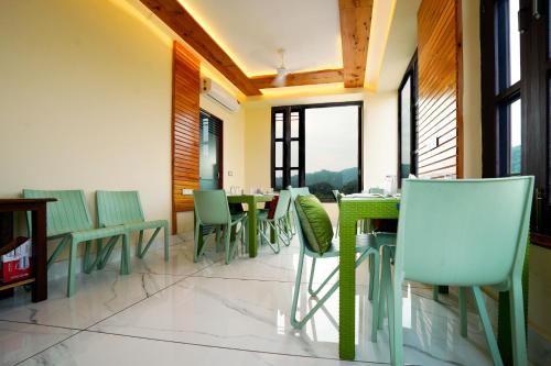 un restaurante con sillas verdes, mesas y ventanas en The Abhyudyam Ganga en Haridwār