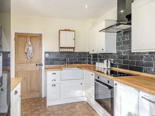 a kitchen with white cabinets and a black tile wall at Kidsty Cottage in Penrith