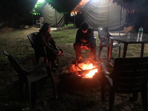 un grupo de personas sentadas alrededor de una fogata por la noche en City Escape Camps and Cafe Kheerganga, en Kheerganga
