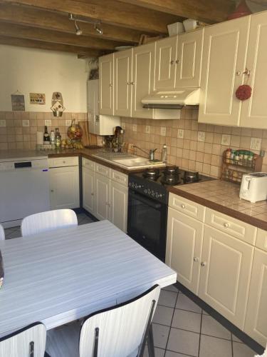 une cuisine avec des armoires blanches et une table avec des chaises dans l'établissement Maison Etretat à 50 mètres de la plage, à Étretat