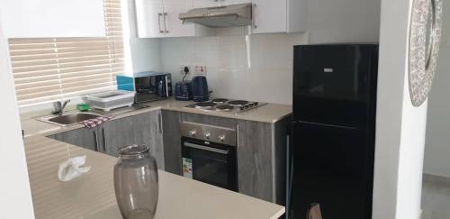 a small kitchen with a black refrigerator and a sink at Sarona city Habitat Alpha apartments C202 Gaborone in Gaborone