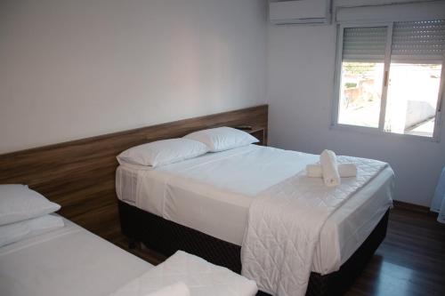 Habitación de hotel con 2 camas con sábanas blancas en Hotel Palmeiras, en Santana do Livramento