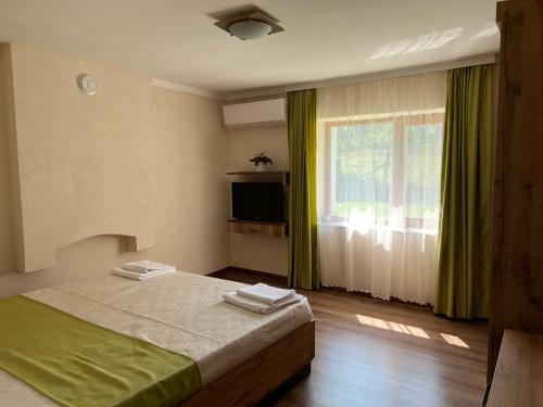 1 dormitorio con 1 cama y una ventana con cortinas verdes en Къща Ралица, en Chakalarovo