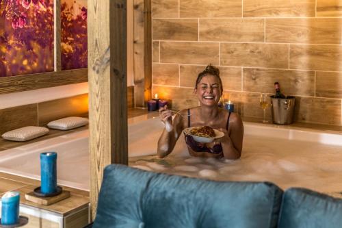 a woman holding a plate of food in a bathtub at Das Aunhamer Suite & Spa Hotel in Bad Griesbach