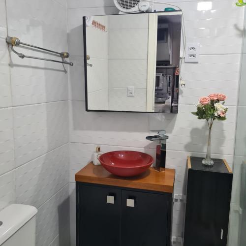 a bathroom with a red sink and a mirror at Kitnet casal e apartamento com lareira e vista jardim in Esteio