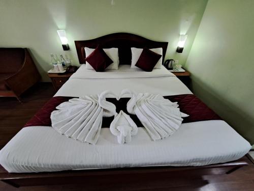 a bedroom with a bed with white comforter and two wings at Hotel Preethi Classic Towers in Ooty