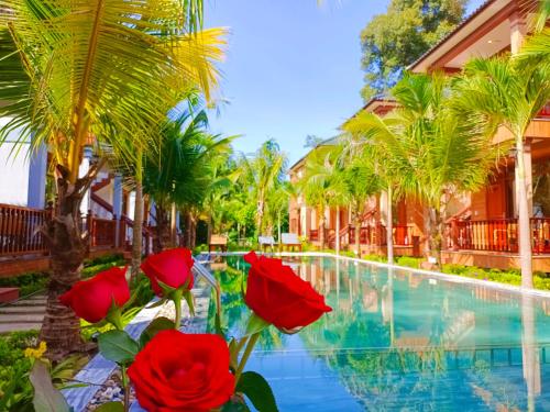 a resort pool with red flowers and palm trees at Valentina Resort & Spa Phu Quoc in Phu Quoc