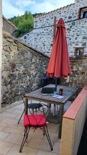 un tavolo con ombrellone rosso e sedia di L'Esprit du vallon de Berlou a Berlou