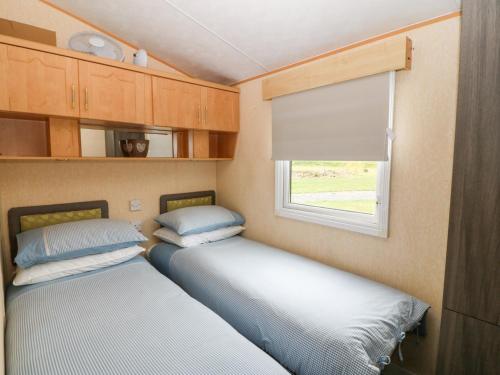 Duas camas num pequeno quarto com uma janela em Plas Tirion Caravan em Holyhead