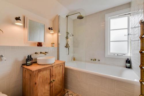 een badkamer met een bad, een wastafel en een raam bij Cheerful 3 bed Grade II Central Cottage in Cirencester