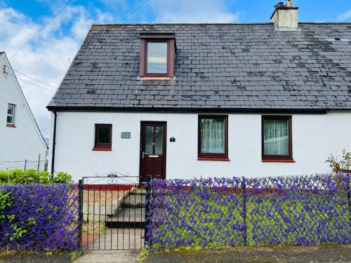 a white house with purple flowers in front of it at Skye View-Skye Bridge House in Kyle of Lochalsh