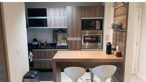 a kitchen with a wooden table and two white stools at Apartamento Executivo - No melhor lugar do América in Joinville