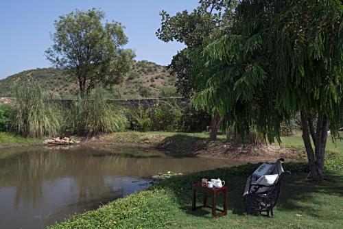 a bench next to a pond with a table next to it at Sariska Manor Luxury Cottages Tehla in Tehla