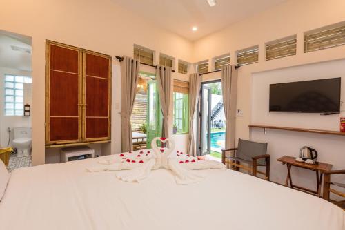 a bedroom with a large white bed with a flat screen tv at Hoi An Wanderlust - Beachside in An Bang